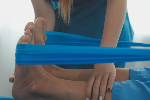Professional orthopedist examining the little patient's leg in the clinic. Patient at the physiotherapy doing physical exercises with his therapist